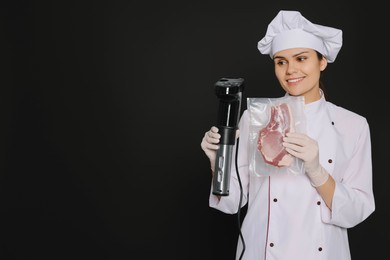 Photo of Chef holding sous vide cooker and meat in vacuum pack on black background. Space for text