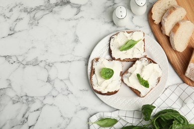 Photo of Bread with cream cheese and basil on white marble table, flat lay. Space for text