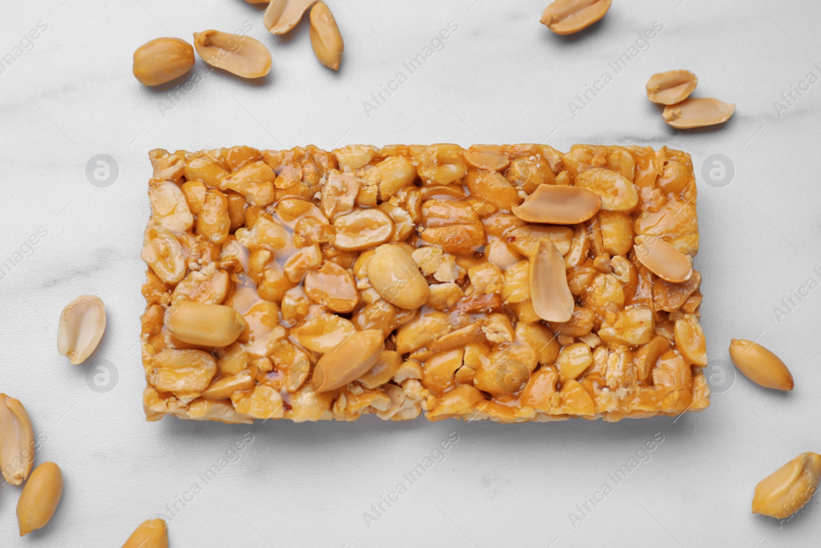 Photo of Delicious peanut bar (kozinaki) and nuts on white marble table, flat lay