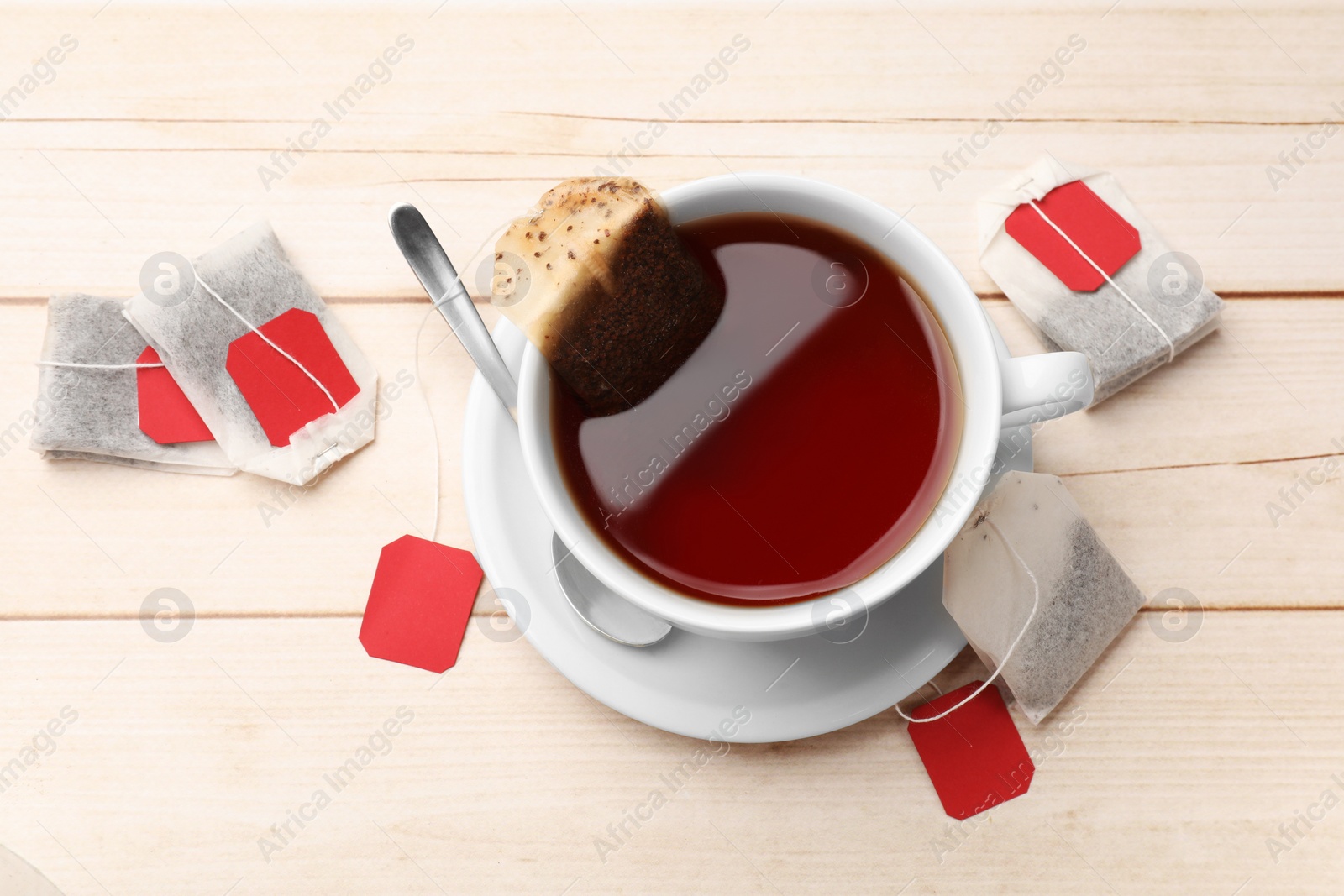 Photo of Tea bags, cup of hot beverage and spoon on light wooden table, flat lay