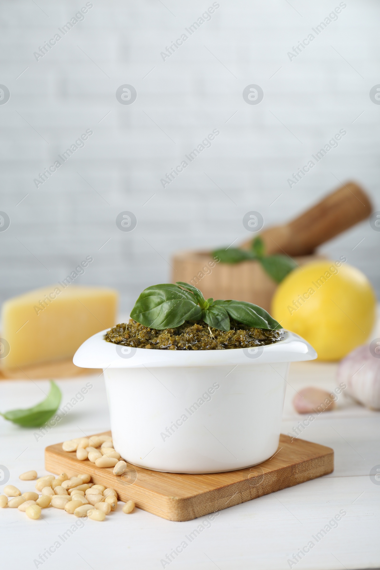 Photo of Delicious pesto sauce in bowl and ingredients on white table. Space for text