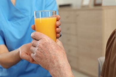 Photo of Nurse giving glass of juice to elderly man indoors, closeup. Assisting senior people