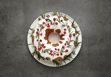 Traditional Christmas cake decorated with glaze, pomegranate seeds, cranberries and rosemary on grey textured table, top view