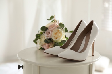 Photo of Pair of wedding high heel shoes and beautiful bouquet on white table, closeup