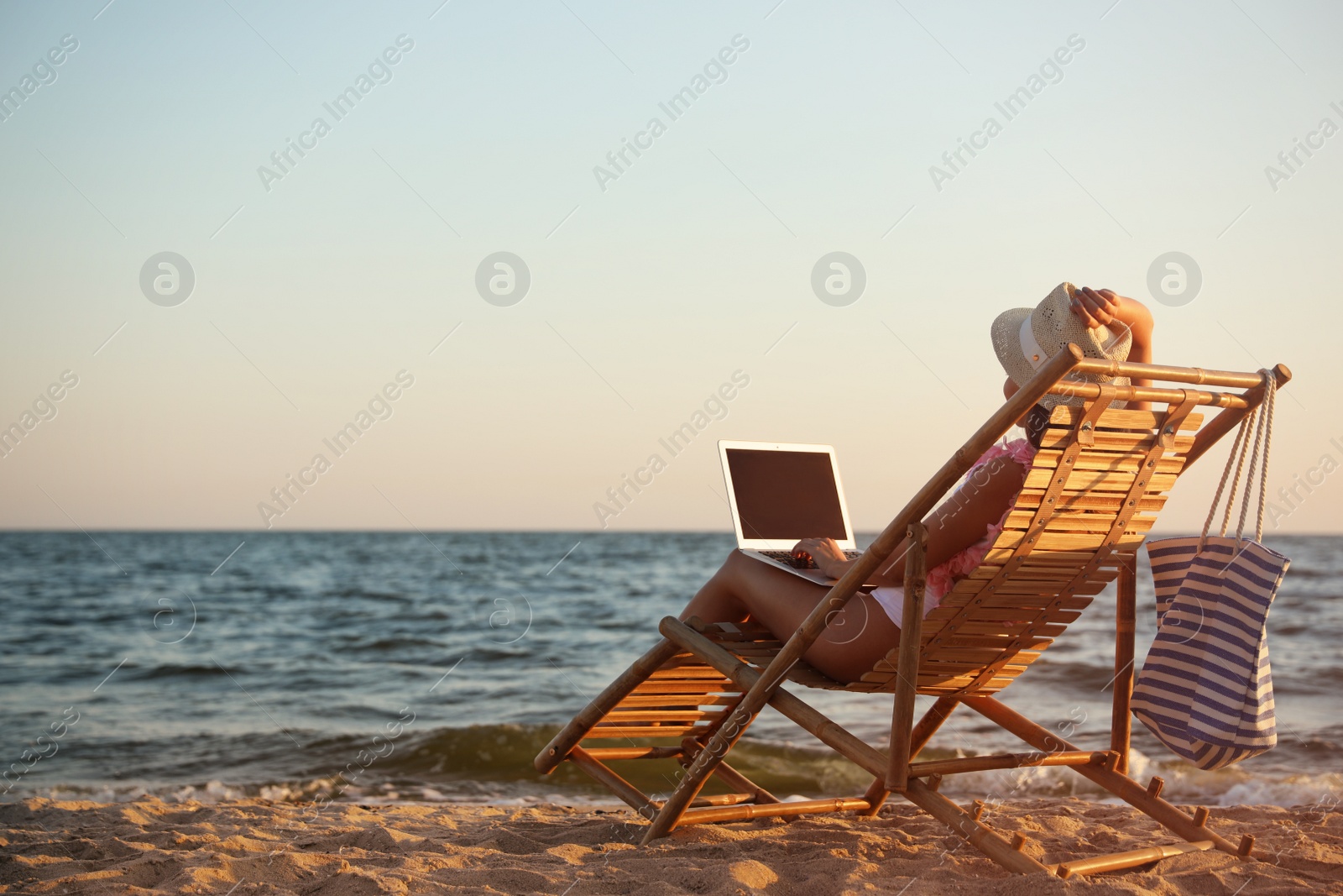 Photo of Young woman with laptop in deck chair on beach