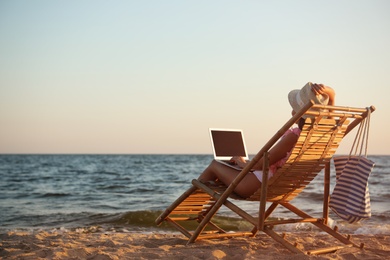 Young woman with laptop in deck chair on beach