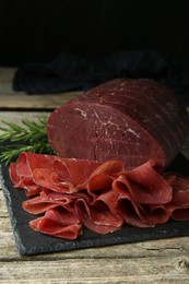 Photo of Tasty bresaola and rosemary on wooden table, closeup