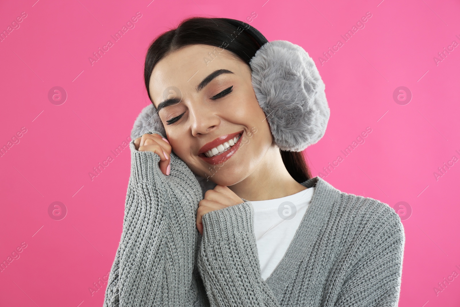 Photo of Beautiful young woman wearing earmuffs on pink background