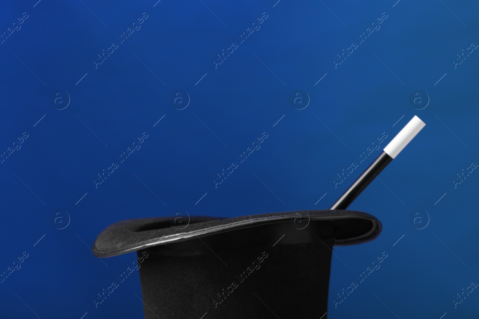 Photo of Magician's hat and wand on blue background, space for text