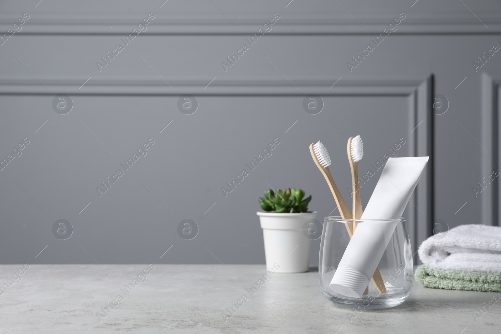 Photo of Bamboo toothbrushes in holder, toothpaste, houseplant and towels on light grey table. Space for text