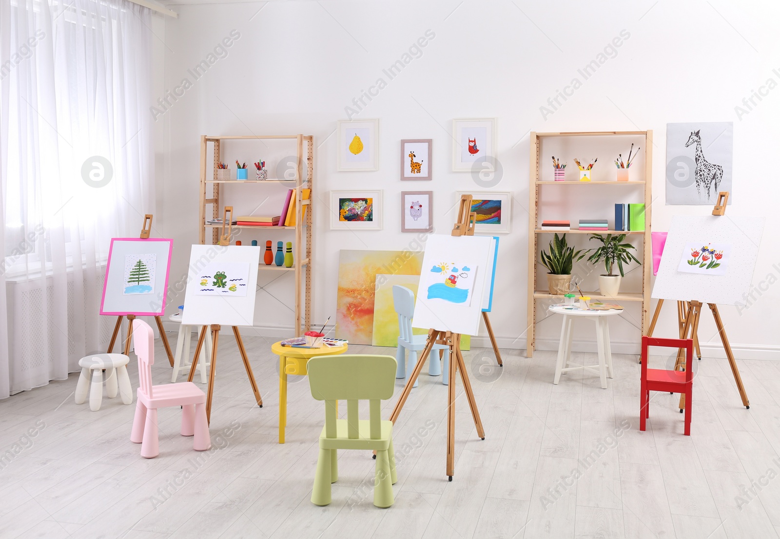 Photo of Easels with paintings and chairs for children in room