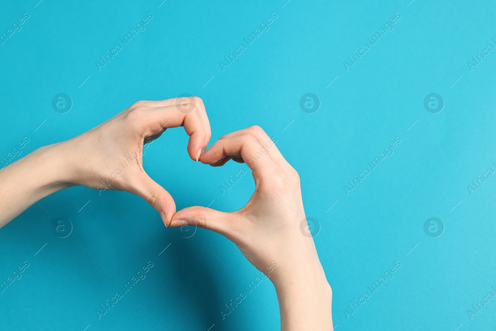 Photo of Woman showing heart gesture with hands on light blue background, closeup. Space for text