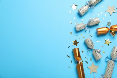 Photo of Open and closed Christmas crackers with shiny confetti on light blue background, flat lay. Space for text
