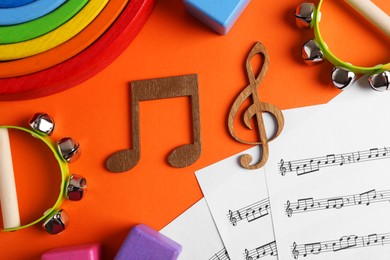 Photo of Tools for creating baby songs. Flat lay composition with wooden notes and tambourines for kids on orange background