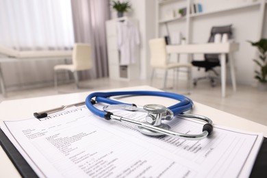 Photo of Clipboard and stethoscope on white table in clinic, closeup with space for text. Doctor's workplace