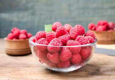 Photo of Delicious fresh ripe raspberries in bowl on wooden table