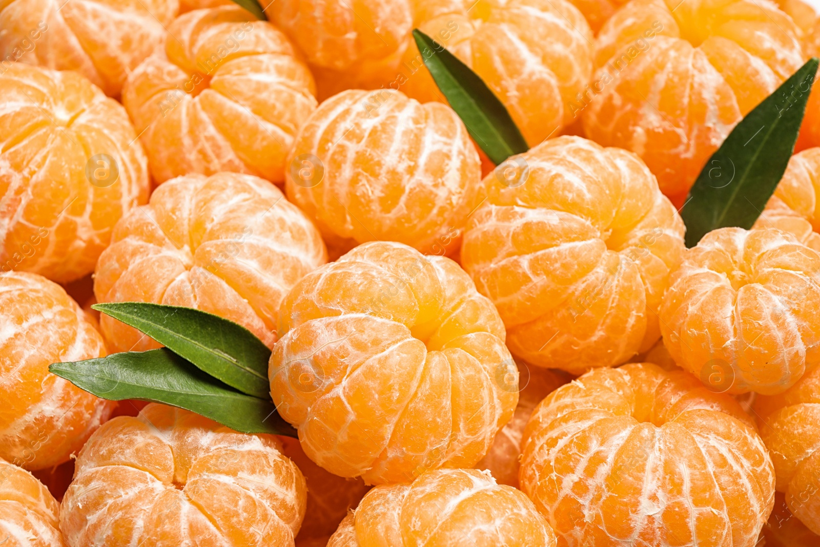 Photo of Peeled fresh ripe tangerines with green leaves as background, closeup