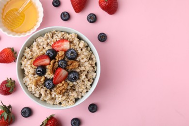 Photo of Tasty oatmeal with strawberries, blueberries and walnuts in bowl surrounded by fresh berries on pink background, flat lay. Space for text