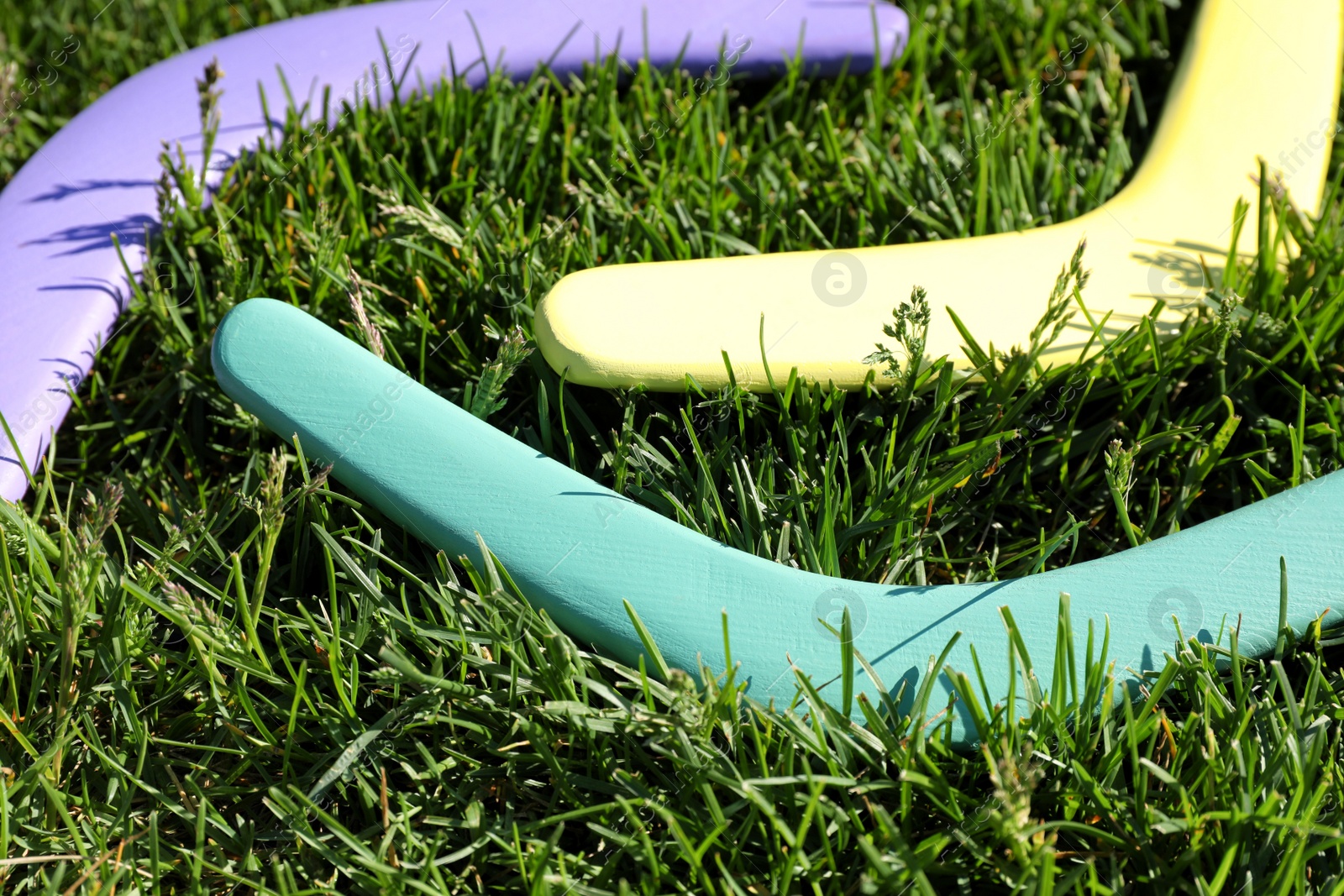 Photo of Turquoise, yellow and violet wooden boomerangs on green grass outdoors, closeup