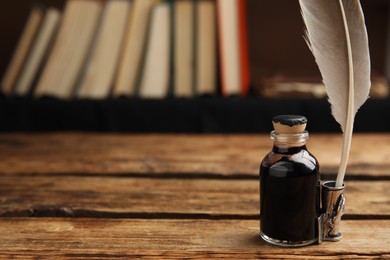 Photo of Feather pen and bottle of ink on wooden table. Space for text