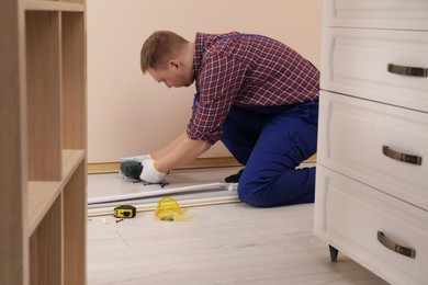 Man installing plinth on laminated floor with screwdriver in room