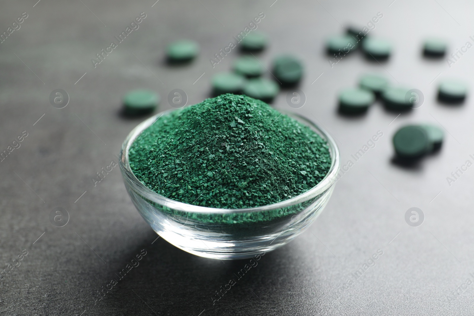 Photo of Bowl of spirulina algae powder on table near pills