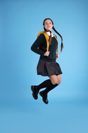 Photo of Teenage girl in school uniform with backpack jumping on light blue background