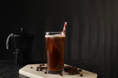 Refreshing iced coffee with milk in glass and beans on table against dark gray background