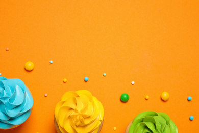 Photo of Colorful birthday cupcakes on orange background, flat lay. Space for text