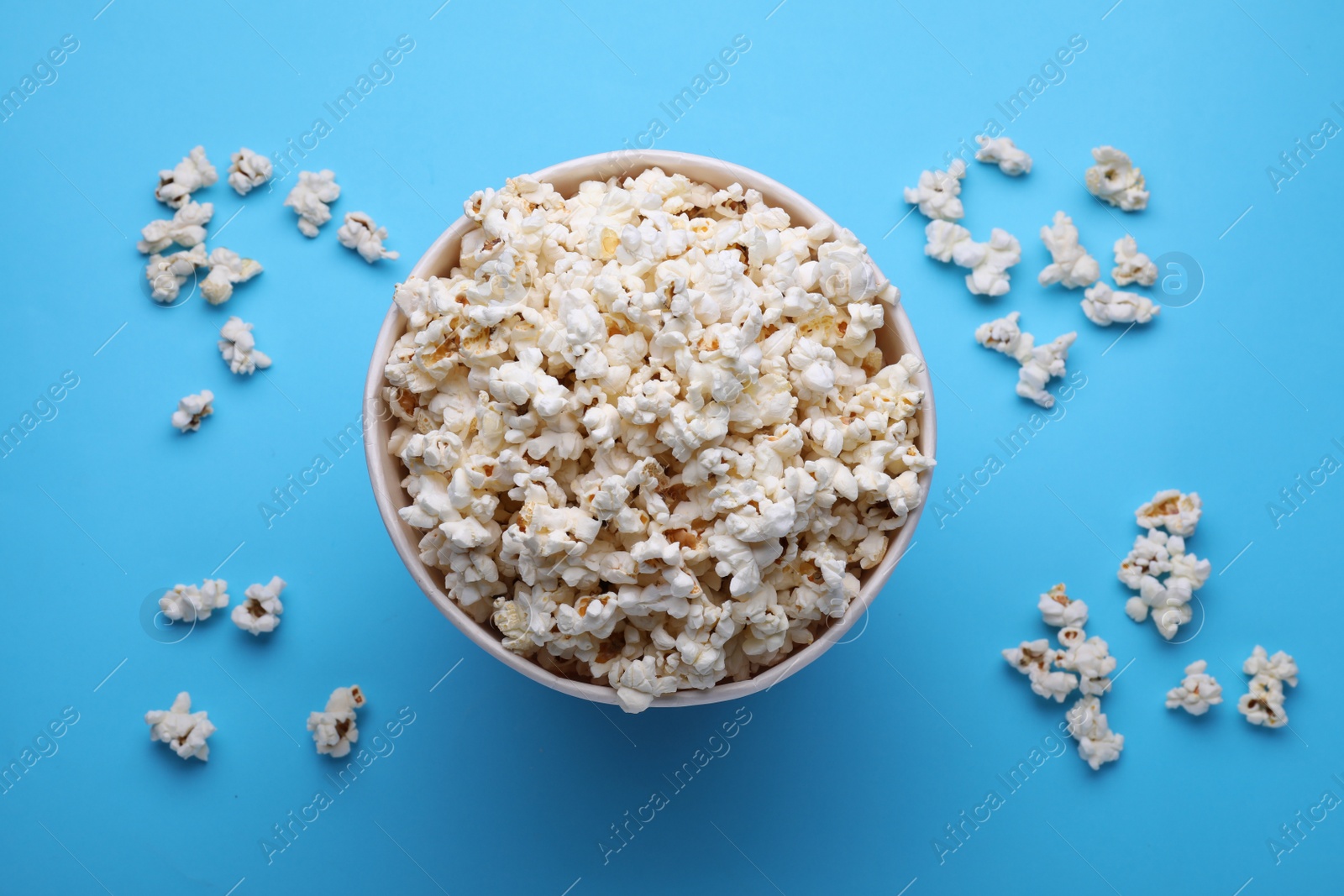 Photo of Paper bucket with delicious popcorn on light blue background, flat lay
