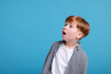Surprised little boy on light blue background, space for text