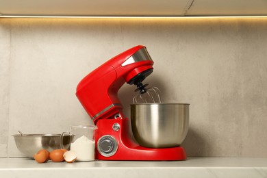 Photo of Modern red stand mixer, eggs, container with flour and bowl on white marble countertop in kitchen. Space for text