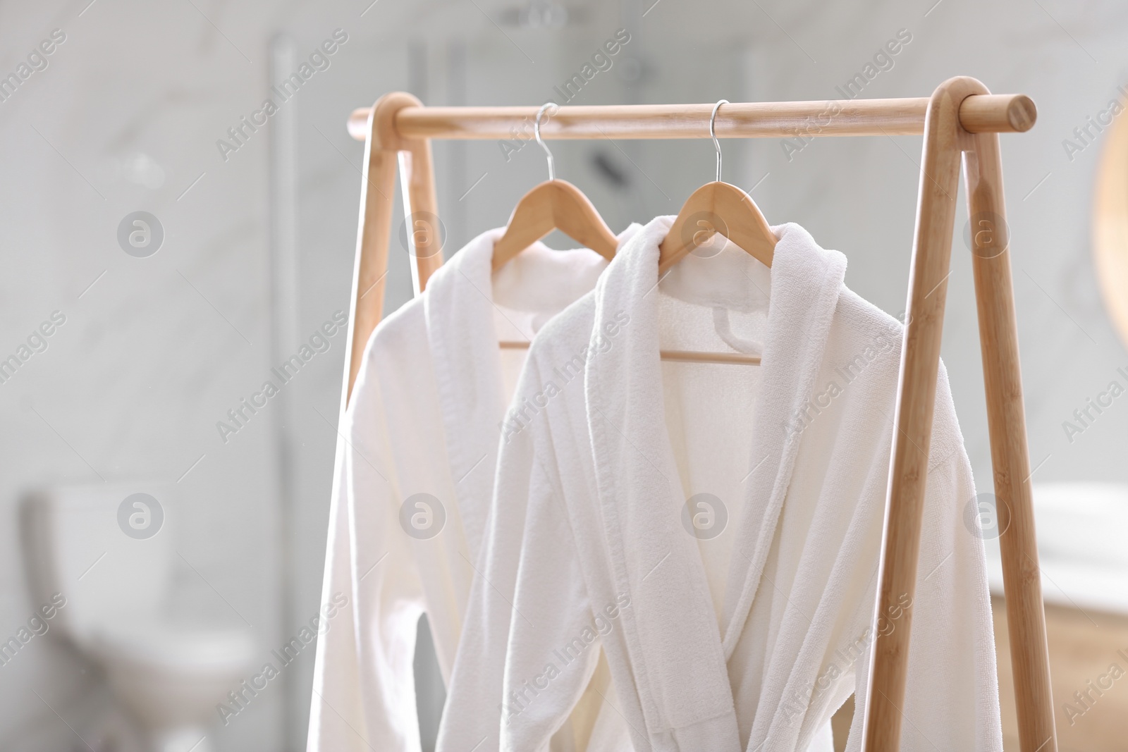 Photo of Fresh white bathrobes hanging on rack indoors