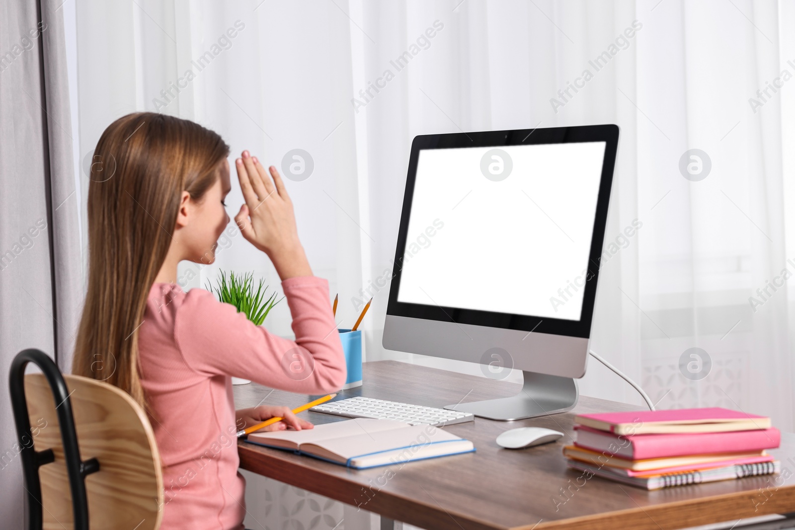 Photo of E-learning. Girl raising her hand to answer during online lesson at table indoors