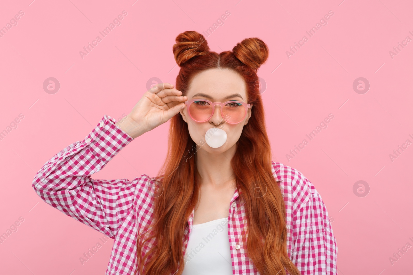 Photo of Beautiful woman with bright makeup blowing bubble gum on pink background