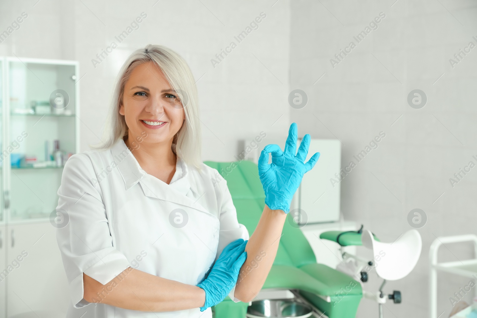 Photo of Smiling gynecologist showing OK gesture at workplace in clinic. Space for text