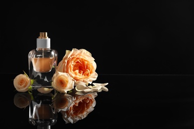 Elegant bottle of perfume and beautiful flowers on black background. Space for text