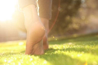 Photo of Young woman walking barefoot on fresh green grass, closeup