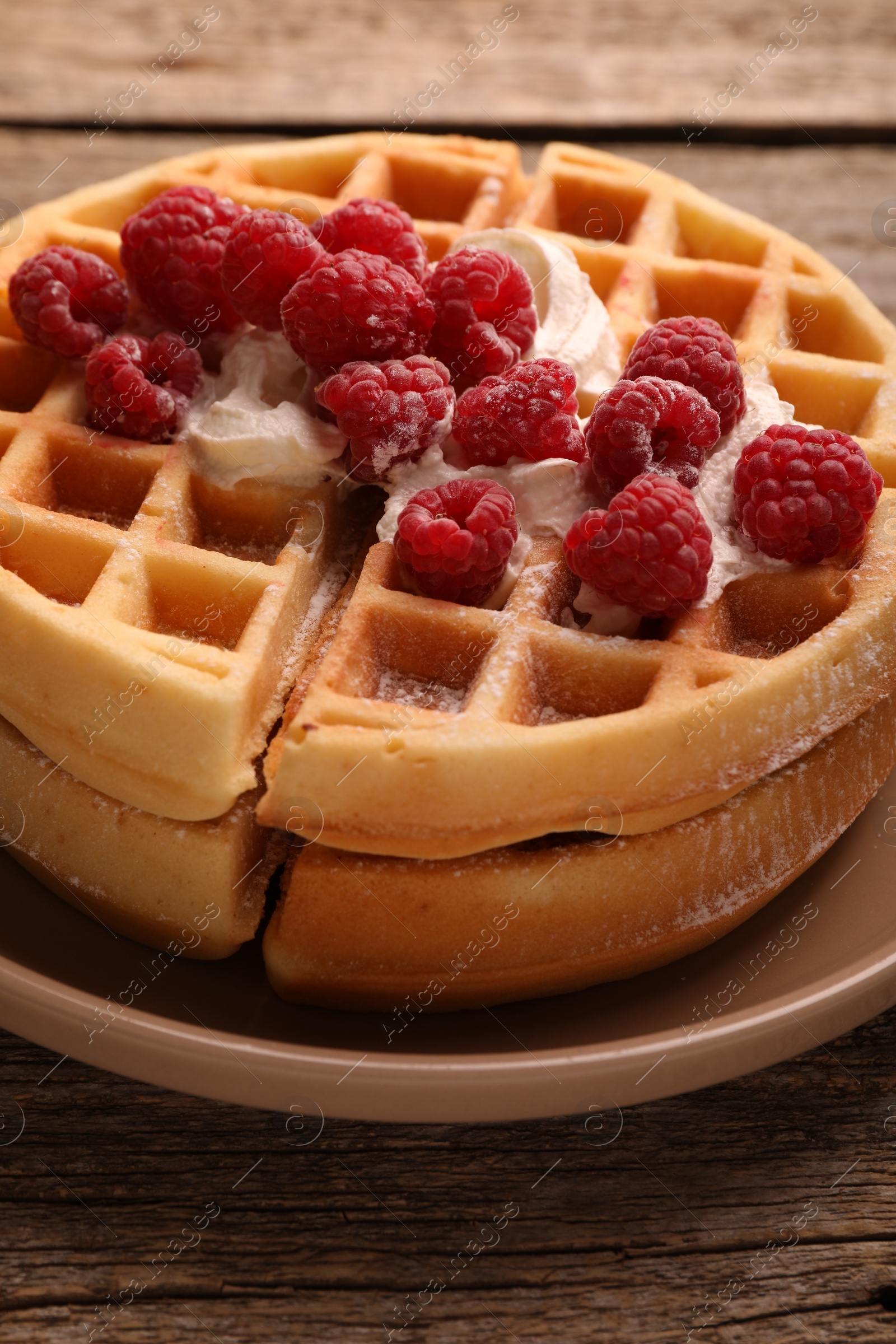 Photo of Tasty Belgian waffles with fresh raspberries and whipped cream on wooden table, closeup