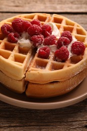 Tasty Belgian waffles with fresh raspberries and whipped cream on wooden table, closeup