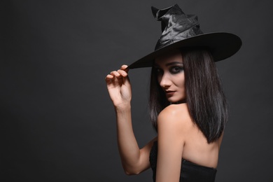 Photo of Mysterious witch wearing hat on black background, space for text