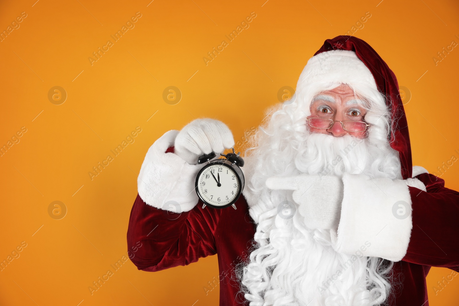 Photo of Santa Claus holding alarm clock on yellow background, space for text. Christmas countdown