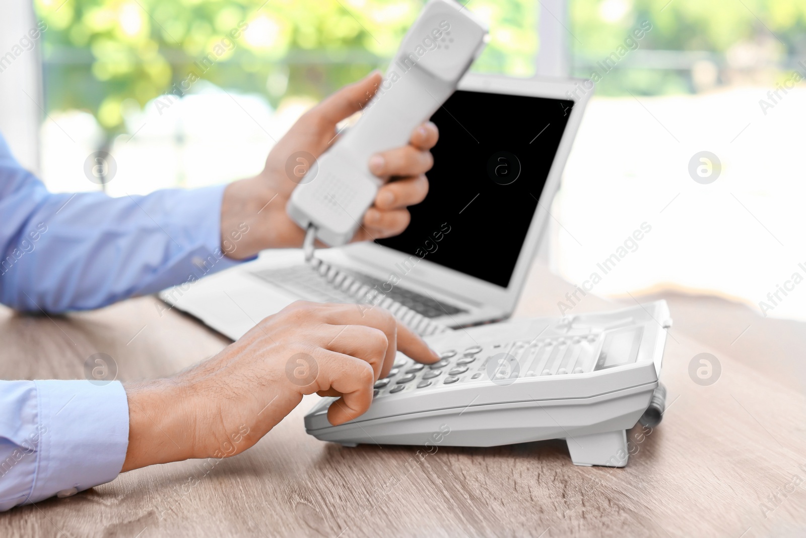 Photo of Man dialing number on telephone at workplace