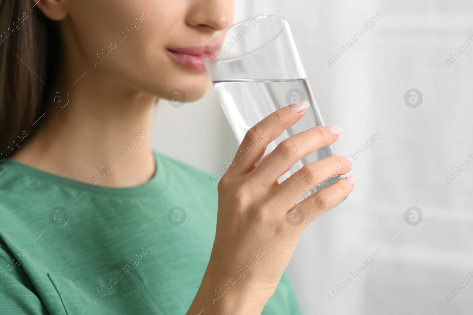 Photo of Healthy habit. Woman drinking fresh water from glass indoors, closeup