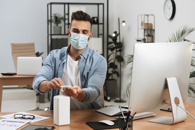 Photo of Man applying hand sanitizer at workplace in office. Personal hygiene during Coronavirus pandemic