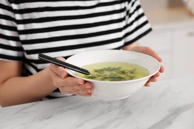 Woman holding bowl with tasty soup at white marble table, closeup