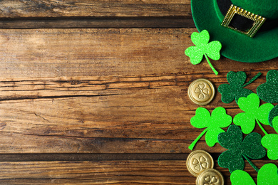 Photo of Green leprechaun hat, clover leaves and gold coins on wooden table, flat lay with space for text. St. Patrick's Day celebration