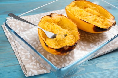 Photo of Halves of cooked spaghetti squash and fork in baking dish on turquoise wooden table, closeup