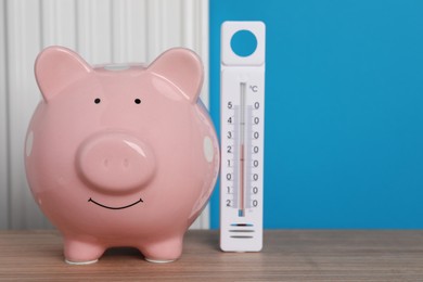 Piggy bank with thermometer on wooden table near heating radiator. Space for text