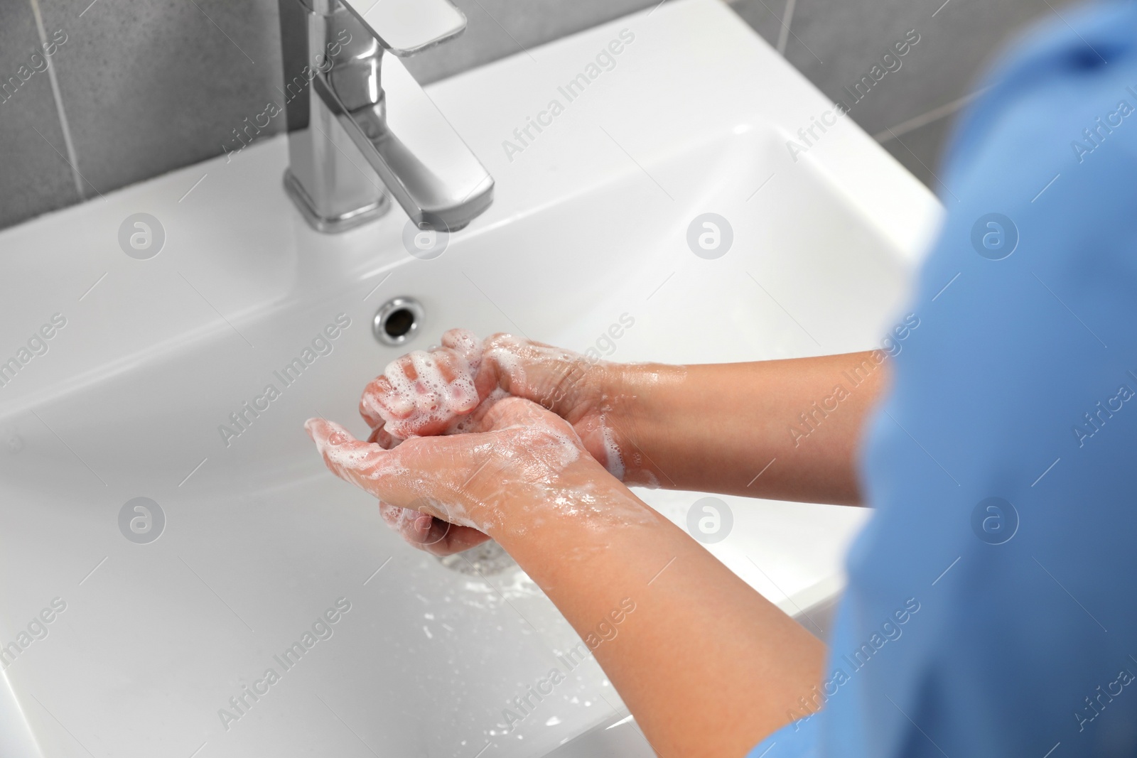 Photo of Doctor washing hands with water from tap in bathroom, closeup